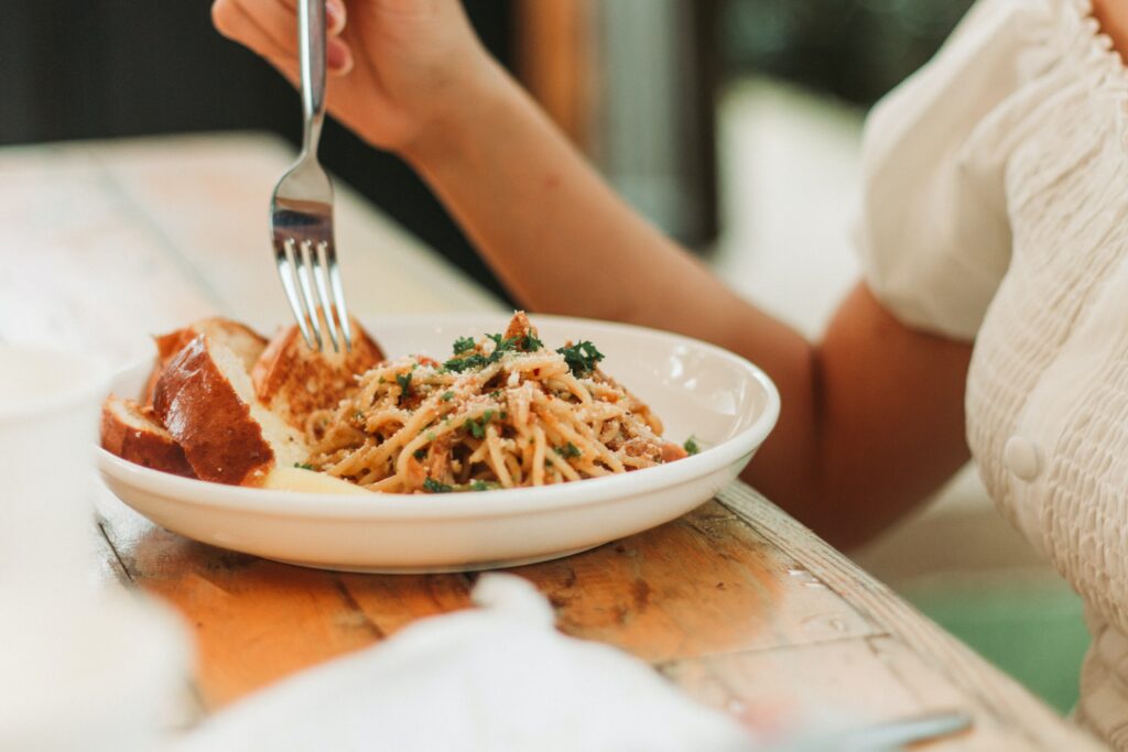 Plate with pasta carbonara, person eating it with a fork